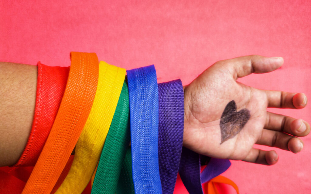 hand with a rainbow of ribbons on arm with a heart drawn on open hand